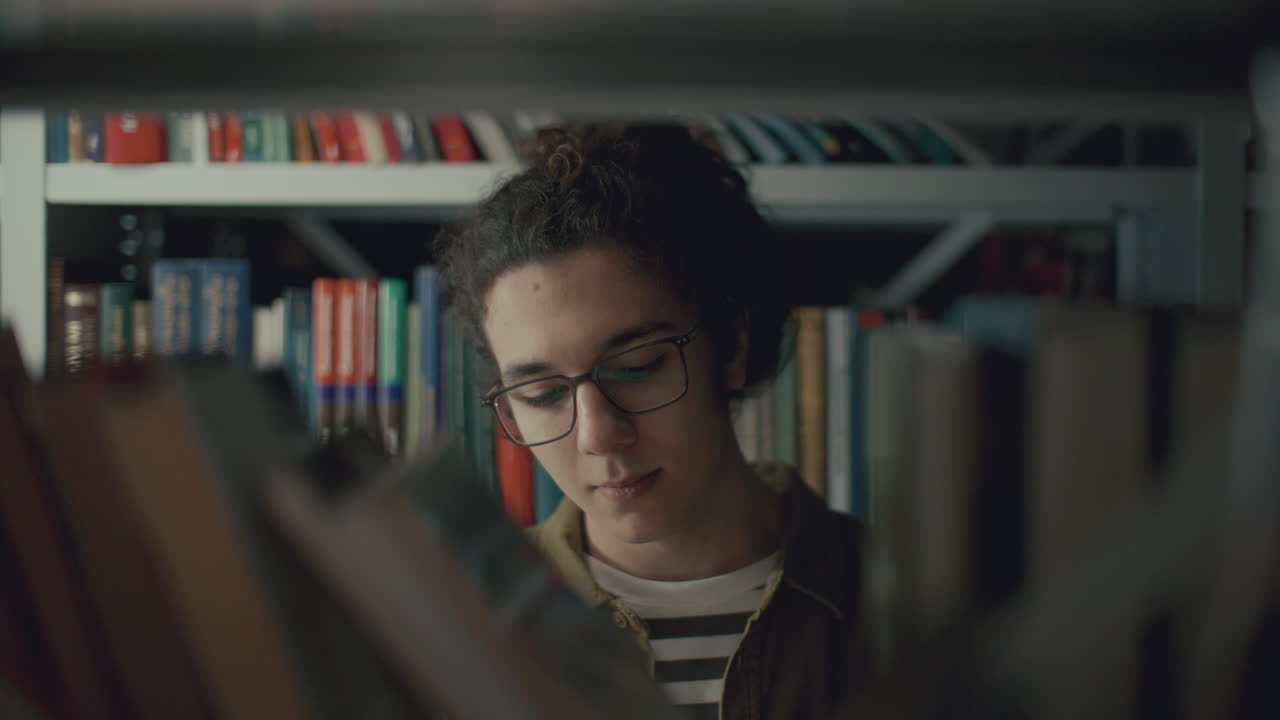 joven estudiante eligiendo un libro en el estante de la biblioteca de la escuela secundaria