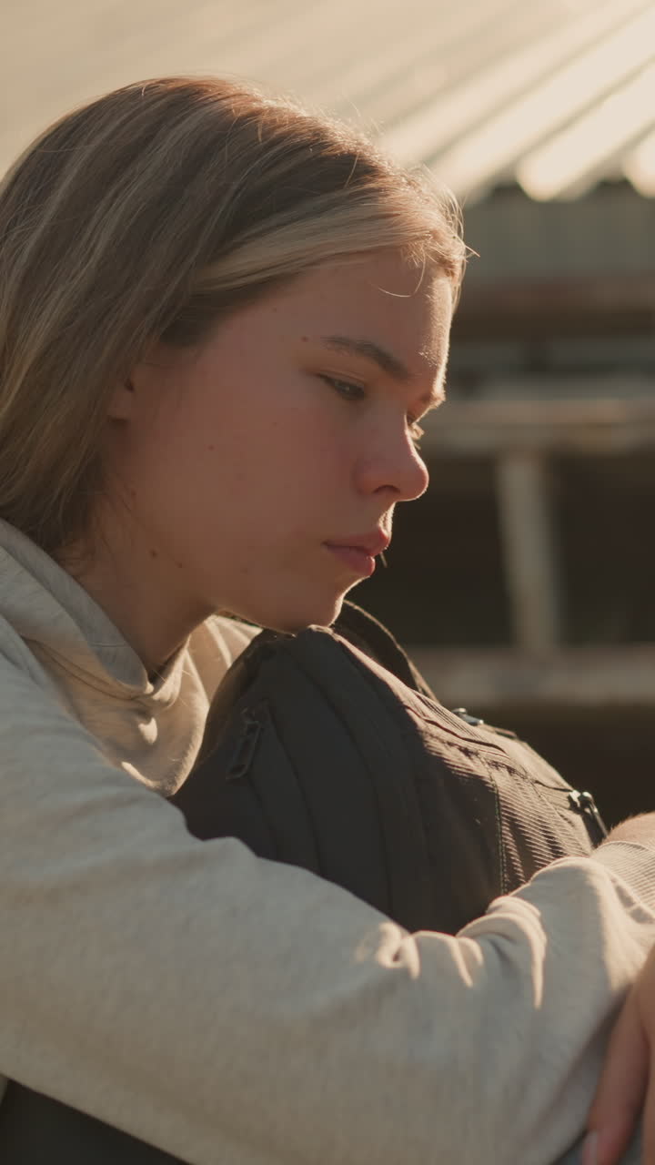 primer plano de una mujer en profundo pensamiento, sentada sola en las gradas vacías del estadio, abrazando su bolsa con una expresión reflexiva e introspectiva, la luz del sol ilumina su rostro