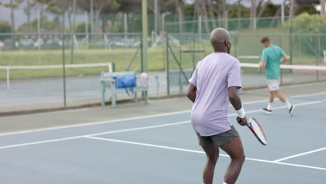 Two-diverse-male-friends-playing-doubles-at-outdoor-tennis-court-in-slow-motion