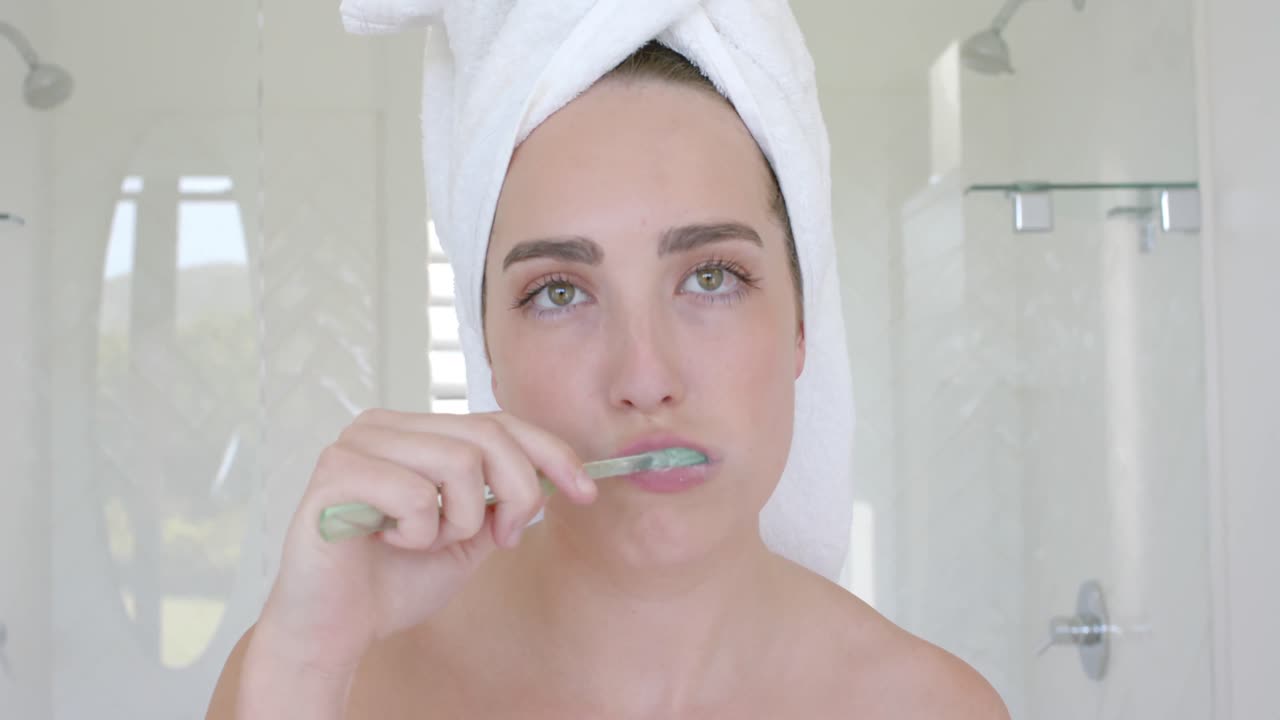 retrato de una mujer caucásica cepillándose los dientes con una toalla en la cabeza en el baño en cámara lenta