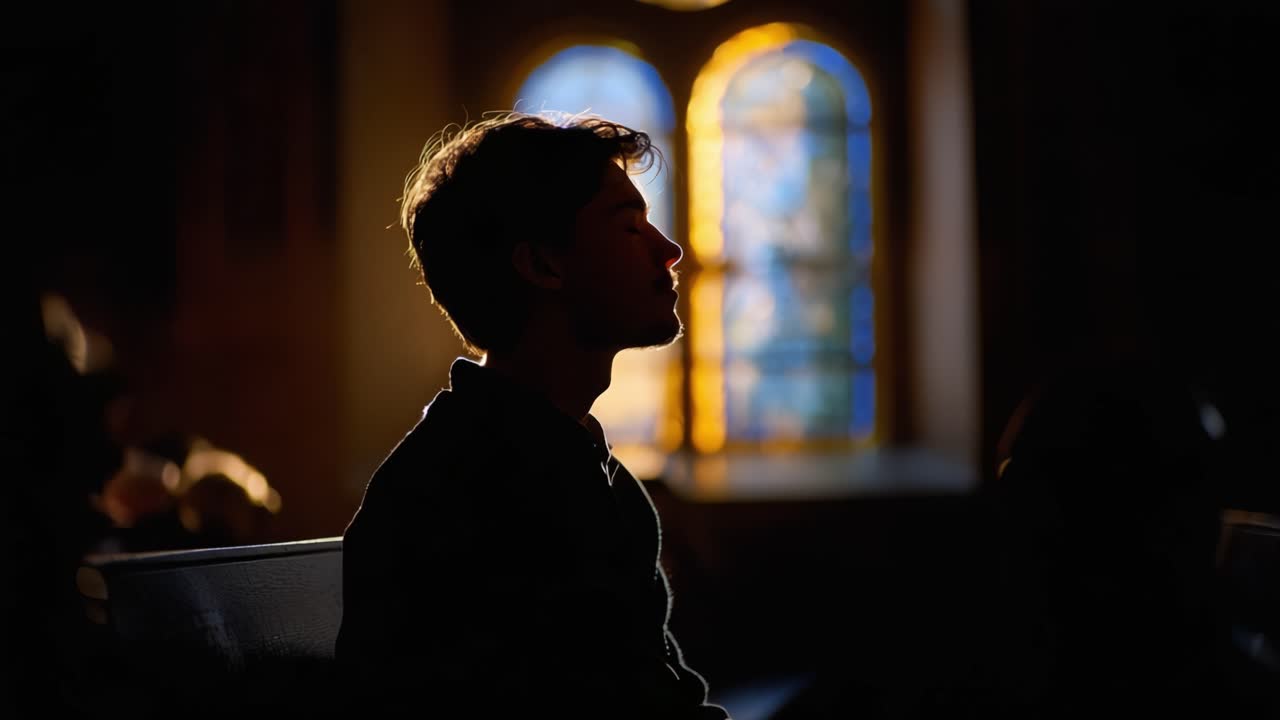 Silhouette di un giovane uomo che contempla in una stanza poco illuminata con una retroilluminazione colorata in vetro piombato che crea un contrasto artistico e profondità