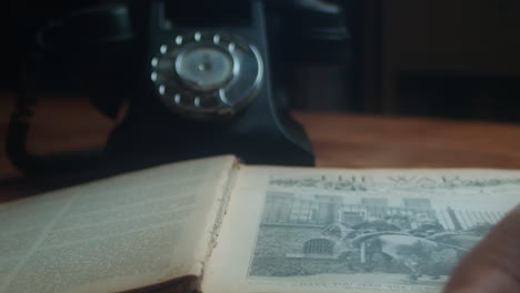 vintage styled scene of someone opening pages of a book while answering an old telephone on the desk