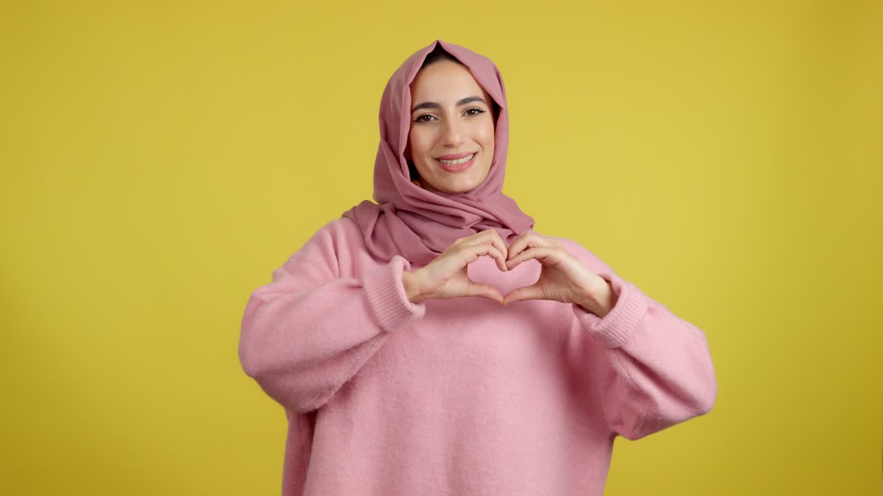 Muslim Woman in Pink Sweater and Hijab Making Heart Gesture