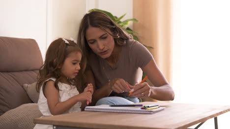 happy mother and daughter drawing in book together at home