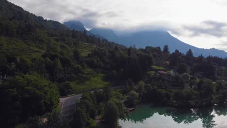 Rising-tilt-down-aerial-footage-at-sunrise-with-Mountain-range-covert-in-Clouds-at-lake-Barcis-Dolomites-northern-italy