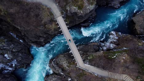 couple standing on impressive bridge over wild river and waterfall in volcanic landscape, aerial top down rotate