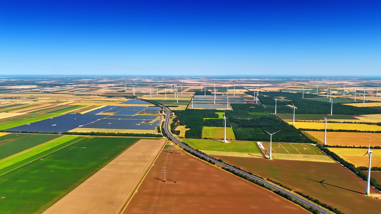 Highway crosses the vast agricultural landscape. Drone footage over the fields with wind turbines and solar panel sites