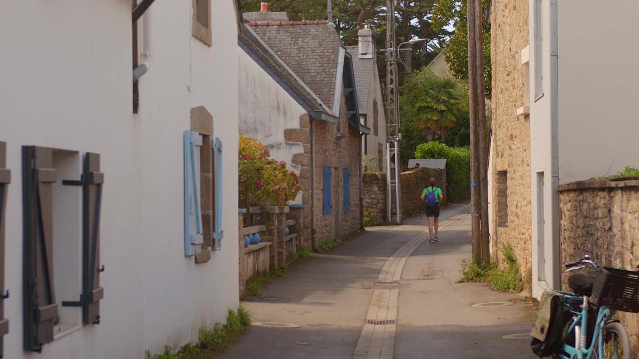 Traveler walking through a narrow traditional street lined with stone houses in Ile aux Moines, Brittany.