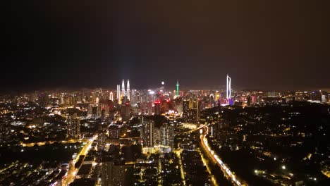 push-in drone shot of kuala lumpur's iconic skyline illuminated by city lights. the glowing petronas twin towers dominate the center, surrounded by high-rise buildings. malaysia