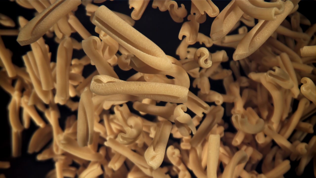 Pasta casarecce secca che cade al rallentatore su sfondo scuro