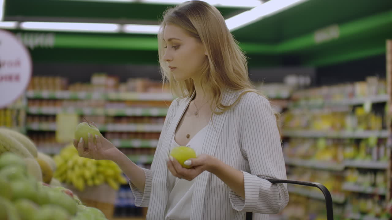 Attractive young woman choosing apple at fruit vegetable supermarket marketplace