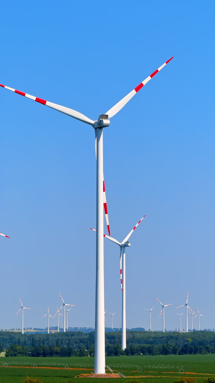 Wind turbines spinning in open landscape. Several wind turbines rotate under a clear blue sky in an open field, showcasing renewable energy in action