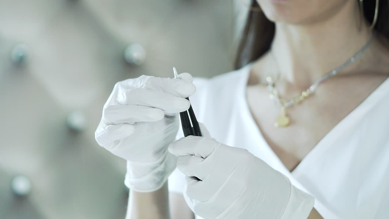 A female beautician in rubber gloves holds a permanent makeup machine. Cosmetology salon