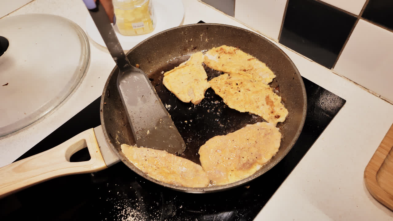 Crispy chicken schnitzels sizzle in pan while flour, grease mark untidy kitchen