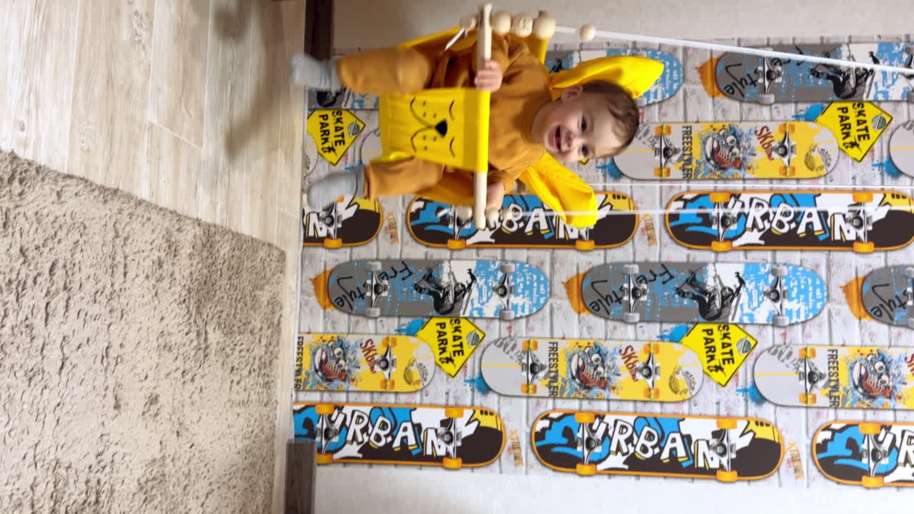 Lovely cute baby in a swing indoors. Baby boy is swinging happily at home. Vertical video.