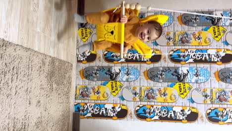 lovely cute baby in a swing indoors. baby boy is swinging happily at home. vertical video.