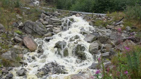 agua de inundación marrón saliendo de una pequeña tubería de drenaje debajo de una carretera noruega - clip estático mirando hacia el río y la valla de la carretera