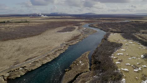 aerial flyover tranquil bruara river surrounded by wide rural landscape in iceland during cloudy day