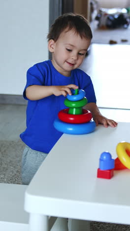 cheerful caucasian baby boy plays at home. smiling kid assembling the toy pyramid on the white desk. top view. vertical video