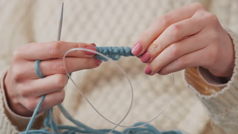 le mani di una ragazza irriconoscibile che lavora a maglia con lana blu 1