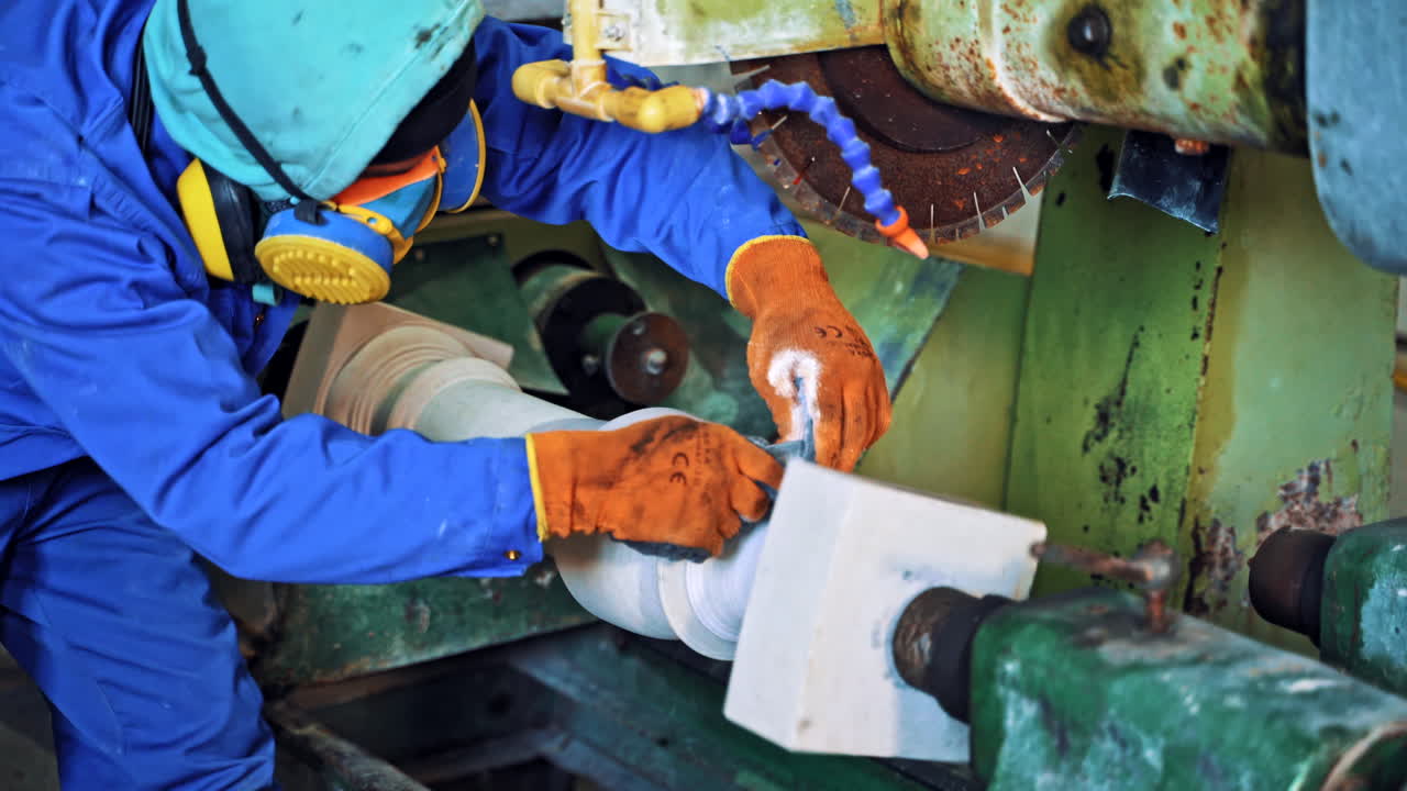 Worker is polishing stone on the industrial machine. Laborer in working clothes grinding rock on the factory background.
