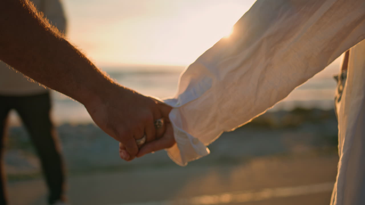 해가 뜨는 해변에서 손을 잡고 데이트하는 연인들. 가까이서. 팔을 만지는 커플