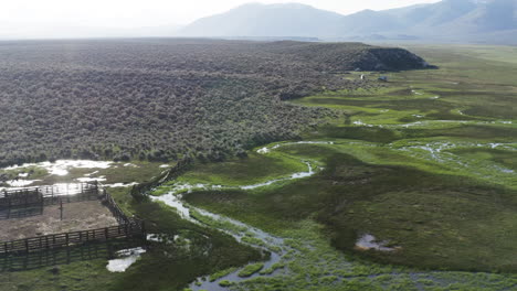 Aerial-footage-showcasing-a-winding-river-meandering-through-lush-green-fields-and-a-rustic-fenced-paddock,-offering-a-picturesque-and-serene-landscape