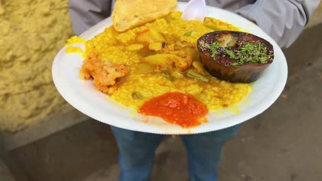 khichuri with begun bhaja, chutney and papad served on a plate by a bengali restaurant.