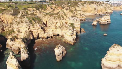 Little-beachlets-and-caves-carved-into-ochre-cliffs-by-the-Algarve-sea,-in-Lagos,-Portugal---Aerial-Crane-down-Reveal-shot