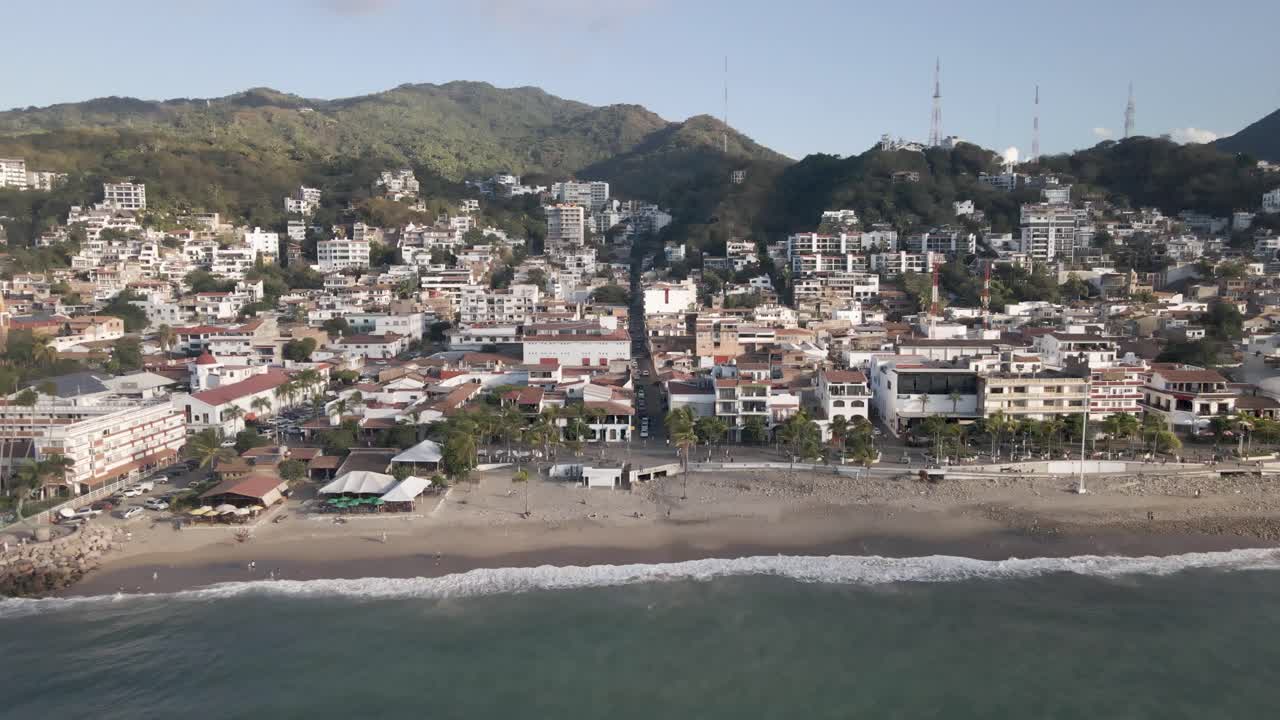 Drone footage unveils the vibrant scene of the Malecon Boardwalk in Puerto Vallarta, Mexico. This bustling seaside promenade becomes the central character in a lively tableau of beachfront city life