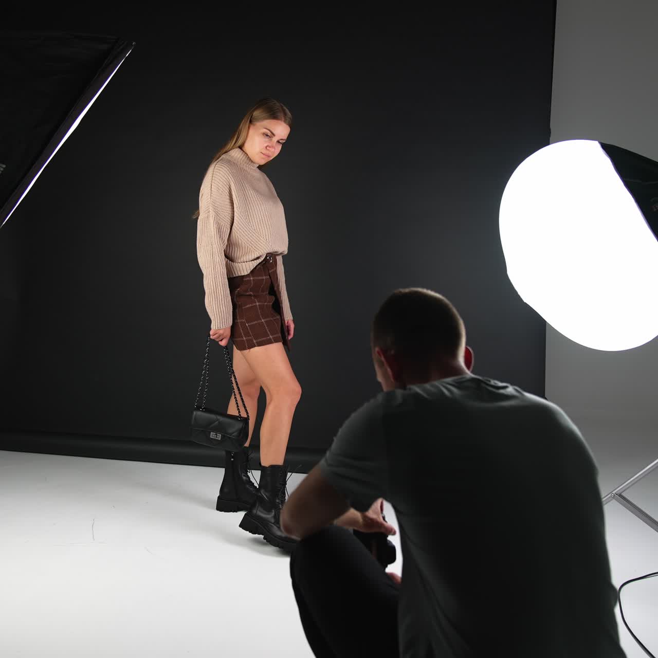 Lady posing in studio for a male photographer. Cameraman squats to find the best angle for photography