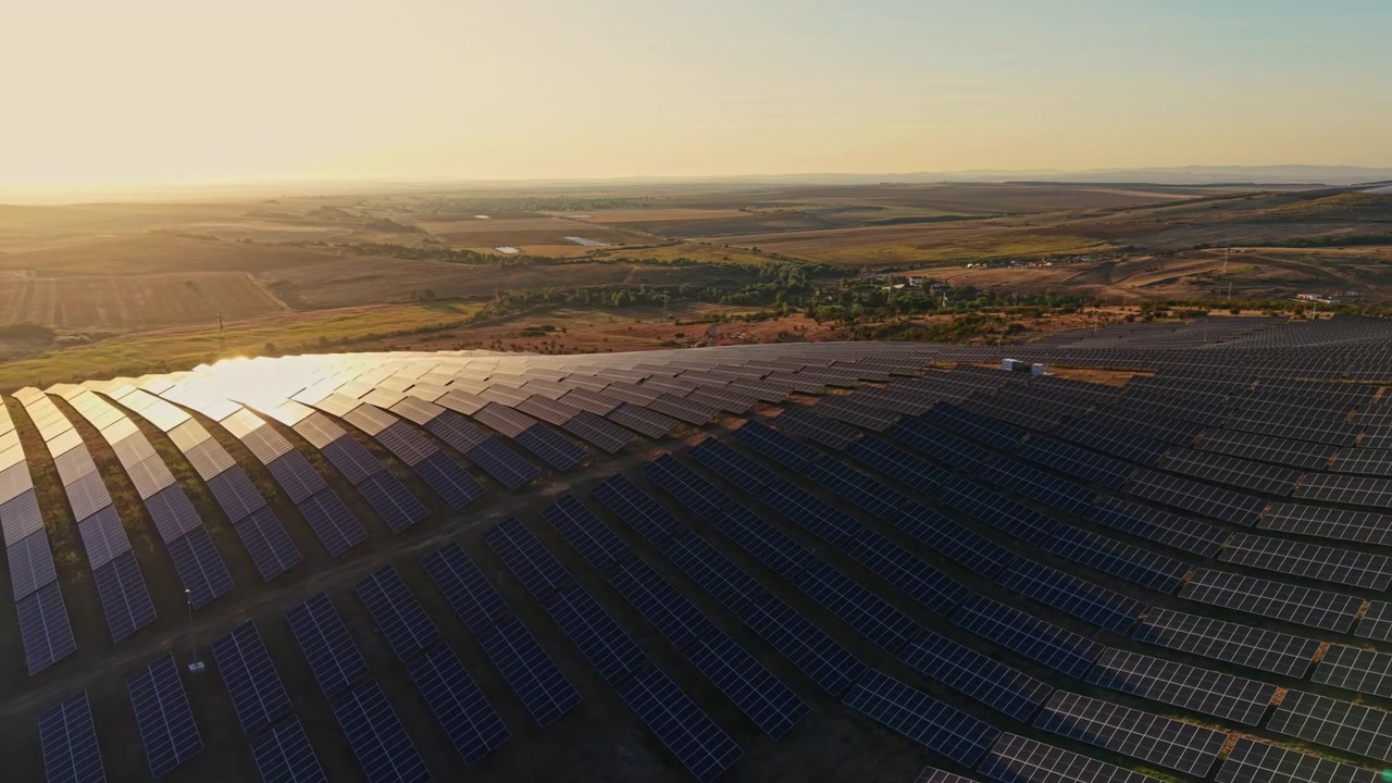 Solpaneler dækker et landskab under solnedgang med bakker og marker i baggrunden
