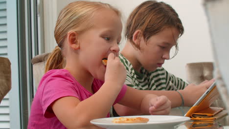 Siblings-enjoying-pizza-and-gadgets