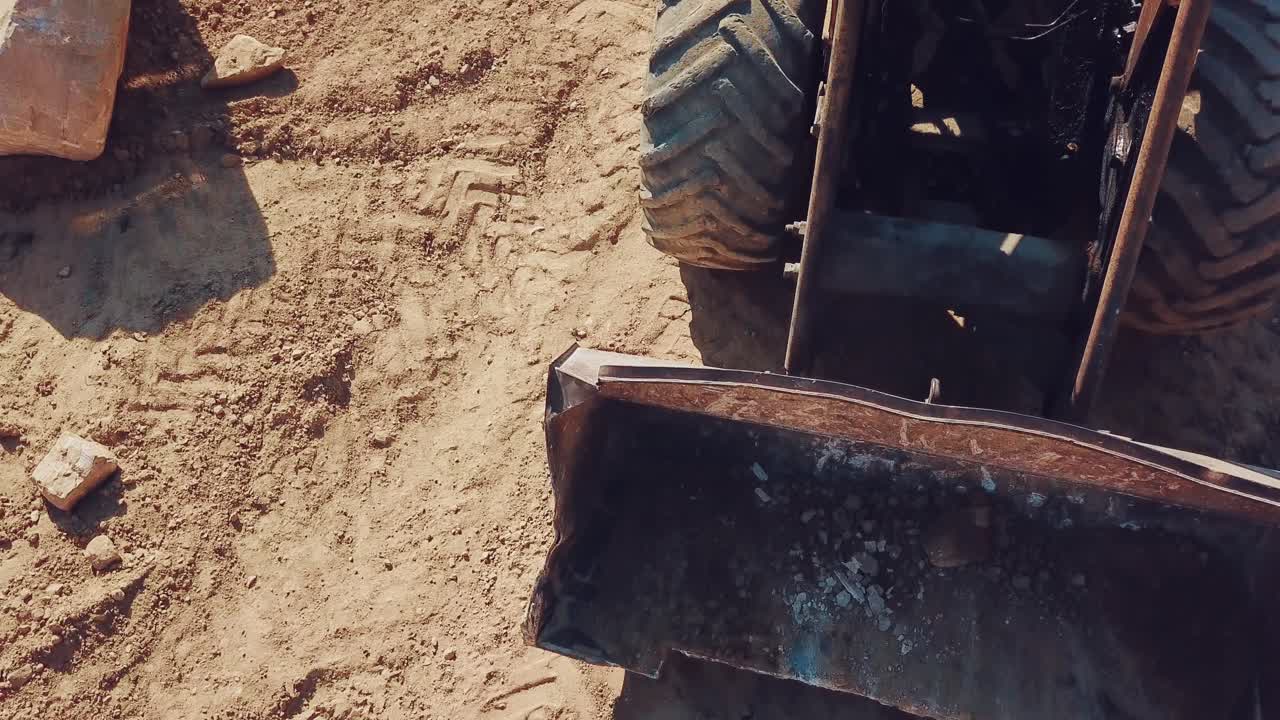 bulldozer with huge wheels and a bucket is moving around the territory of a sandy quarry. Close-up