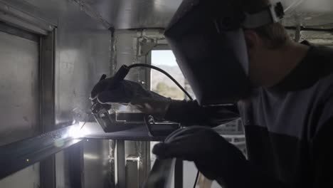 Welder-welding-metal-frame-construction-wearing-shield-mask-indoors--slow-mo