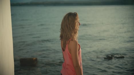 happy blonde woman standing in front of sea and attending around