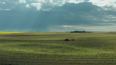 sensational sunlight and beams of light shine on green farm land with tractor traveling on flat farmland in vast countryside on cloudy day, saskatchewan, canada, above aerial sideways