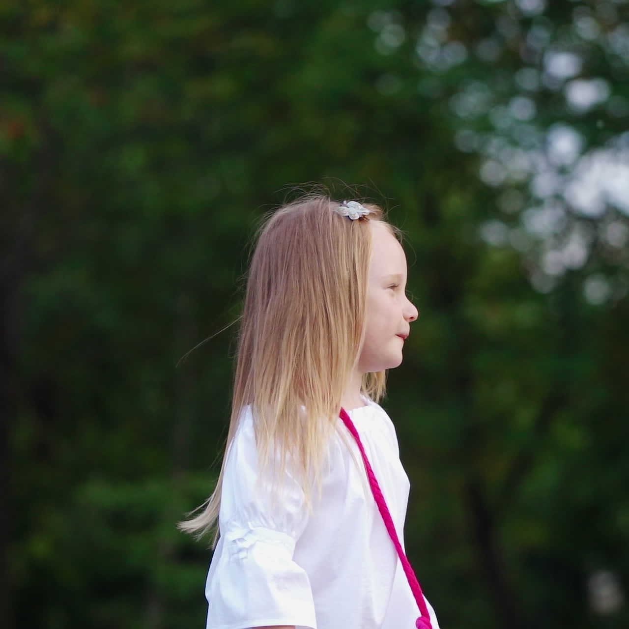 Positive little girl with soap bubbles outdoors. Smiling lovely child with blond hair popping colorful air bubbles in the park. Happy childhood.