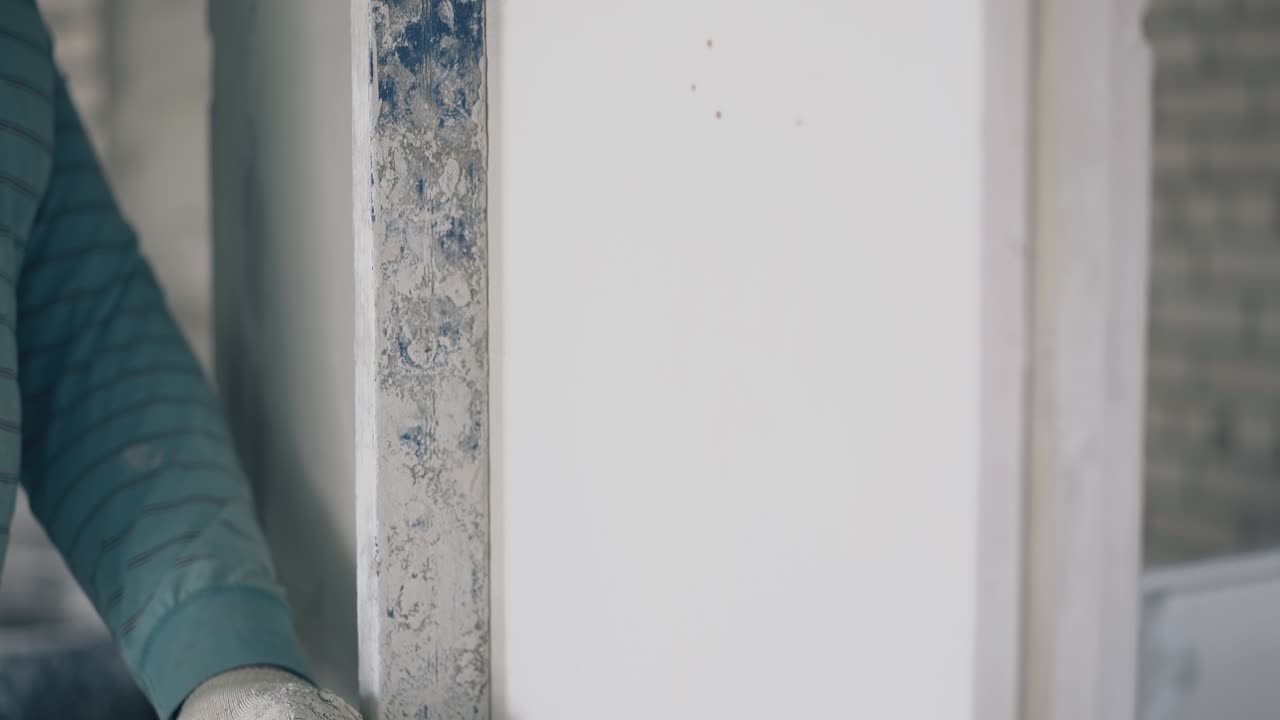 skilled repair worker aligns white gypsum plasterboard wall