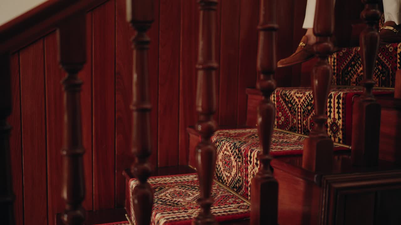 Close up of feet in stylish loafers stepping on patterned carpeted wooden stairs