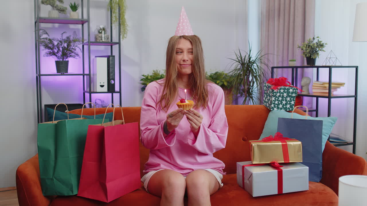 행복한 젊은 여성이 생일파티를 축하하고, 작은 컵케이크에 불타는 불을 불어넣는 소원을 합니다.