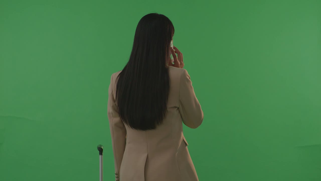 뒷모습 아시아 사업가 여성 여행자, 짐을 들고 스마트폰으로 대화 중, 녹색 스크린 배경 스튜디오에서, 해가 지는 시간