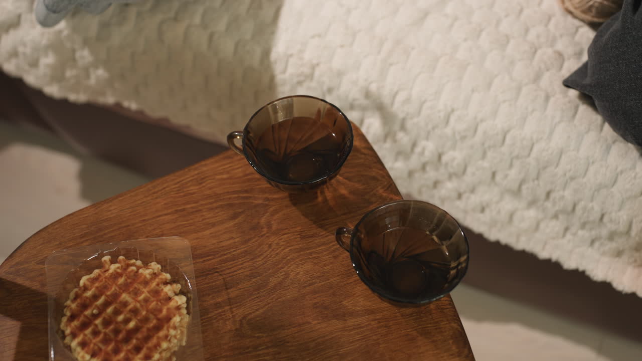 와플이 놓인 찻잔 배치 구도의 오버헤드 뷰. 위에서 촬영한 와플과 함께 차 두 잔이 놓인 장면. 나무 쟁반에 찻잔 두 개와 와플이 놓인 항공 뷰 캡처