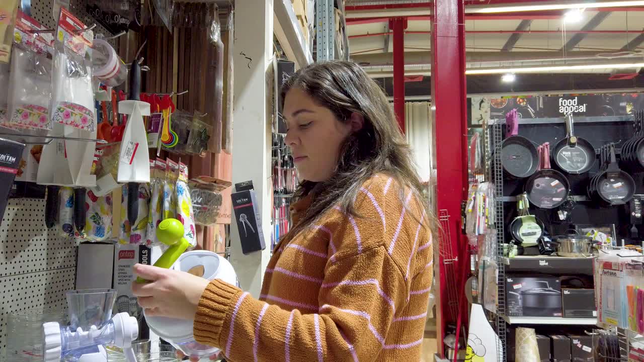 Young woman customer choosing kitchen utensil in shop. Home decor and comfort concept.
