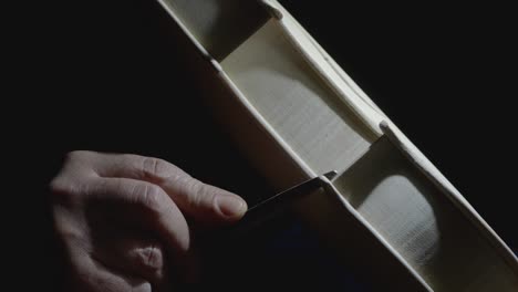 extreme close up macro shot in slow motion of hand of master lute maker smoothing and shaping corner edges near the center bout with raw rasp to new unpainted classical violin