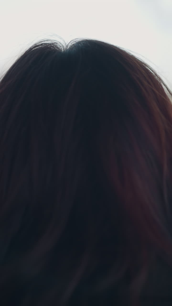 도시 환경에서 바에 서있는 갈색 머리카락을 가진 여성의 뒷면, 그녀의 머리카락과 배경에 부드러운 초점을 맞추고 멀리보고 있습니다.