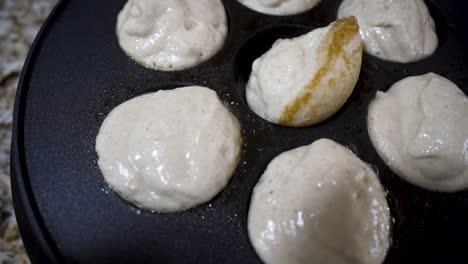 Aebleskiver-In-Einer-Gusseisernen-Pfanne-Drehen,-Während-Sie-Im-Öl-Zu-Einem-Goldenen-Braun-Kochen---Nahaufnahme-In-Zeitlupen-Aebleskiver-Serie