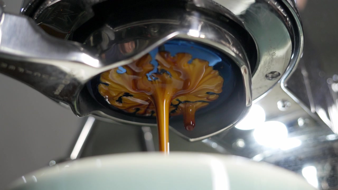 Primo piano che mostra l'estrazione ricca, cremosa e scura dell'espresso da un portafiltro. Perfetto b-roll per caffetterie, routine mattutine e video di servizio barista professionale.