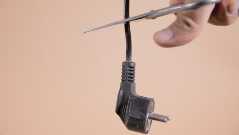 a hand holding a pair of scissors, cutting a hanging black power cord