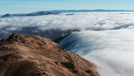 Mountain-peak-towering-above-sea-of-clouds-under-clear-blue-sky,-solitary-figure-in-distance